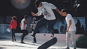 Im Vordergrund ein Jugendlicher, der gerade einen Sprung mit einem Skateboard ausführt. Im Hintergrund: vier weitere Jugendliche.