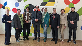 Eine Gruppe von Menschen steht nebeneinander vor einer bunten Wand.