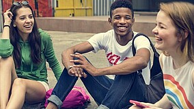 Drei Jugendliche sitzen zusammen auf dem Boden und wirken gut gelaunt.