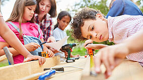 Mehrere Kinder beschäftigen sich gemeinsam mit einer Betreuerin mit Holzarbeiten.