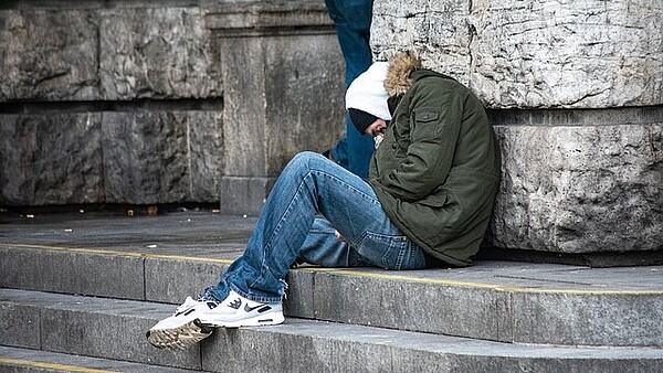 Eine jüngere obdachlose Person sitzt auf einer Treppe.