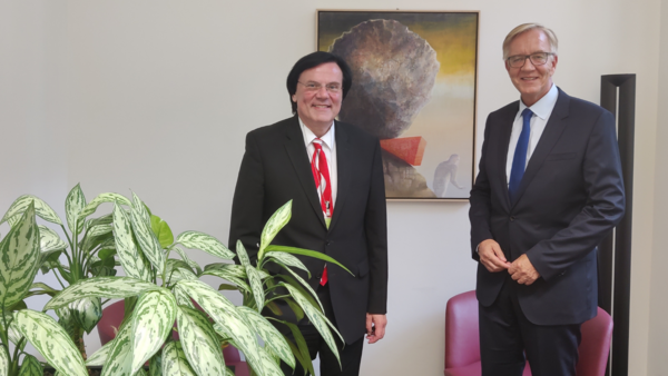 Der IB-Vorstandsvorsitzende Thiemo Fojkar und Dietmar Bartsch, Fraktionschef der Linkspartei im Deutschen Bundestag. Im Vordergrund ist eine Zimmerpflanze zu sehen. An der Wand hängt ein Bild.