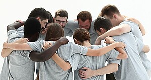 Eine Gruppe Junger Menschen steht im Kreis zusammen und hält sich in den Armen