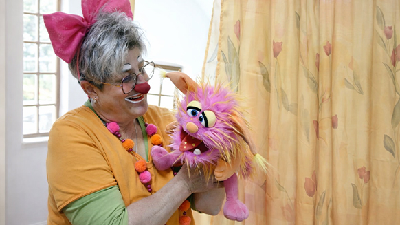 Nicole Hornberger als Clownin &bdquo;Naduli&ldquo; mit Clownsschminke l&auml;chelt und spricht mit ihrer Handpuppe Max Maulich.