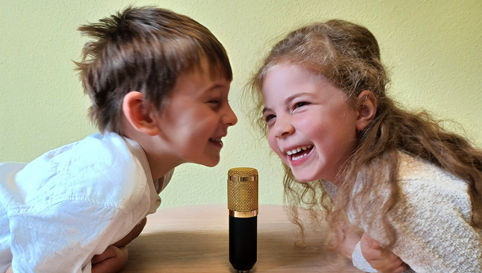 Die Welt mit Kinderaugen hören: Layla und Friedrich moderieren den Podcast „Zwerge auf großem Fuß“. Foto: IB Zwei Kinder sprechen in ein Mikrofon