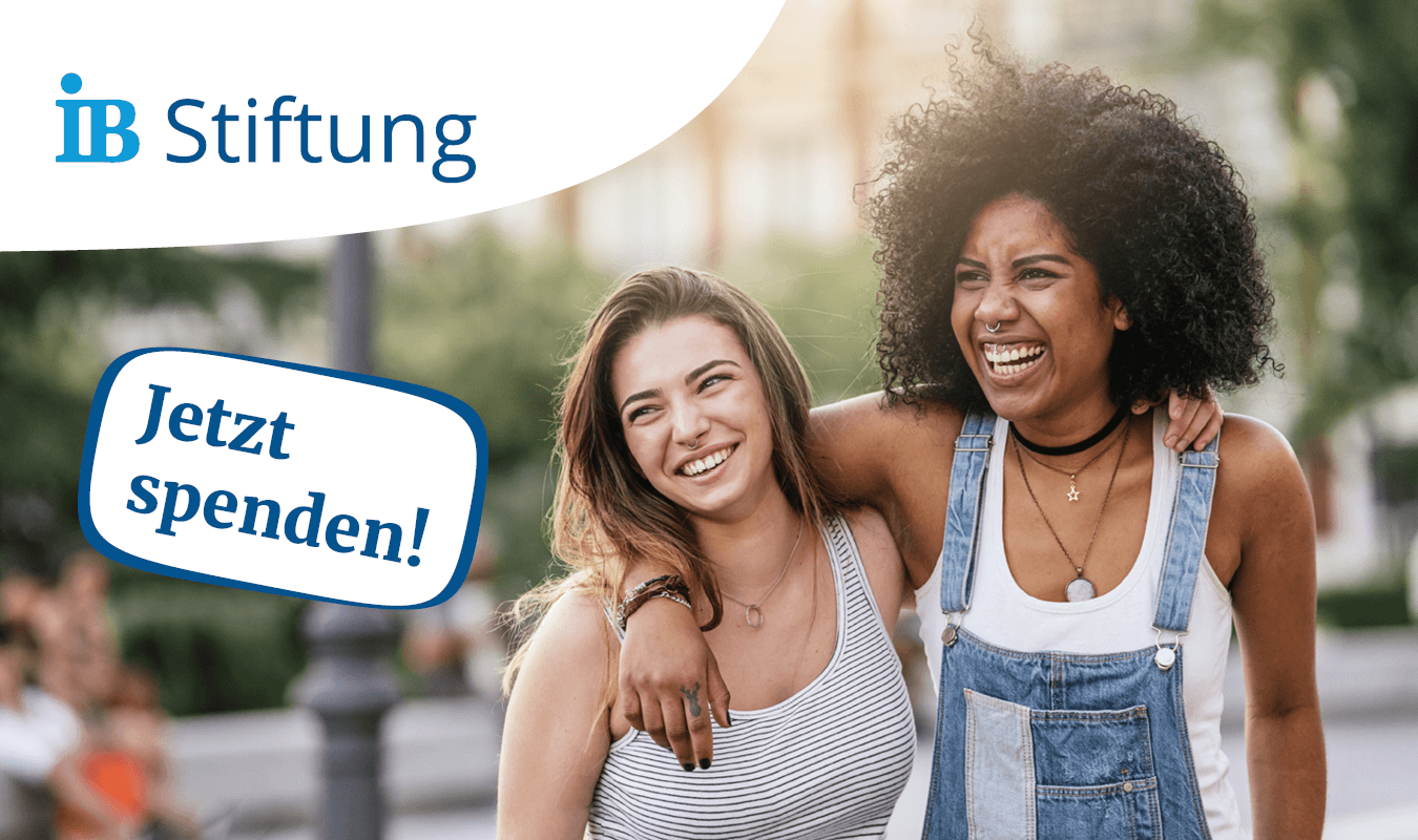 Zwei junge Frauen umarmen sich, eine trägt weiße gestreifte Kleidung, die andere blaue Latzhose, zu sehen ist der Text 'Jetzt spenden!' und das Logo der IB-Stiftung