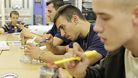 Teilnehmende einer Ausbildung des IB in der Holz- und Metallverarbeitung beim Arbeiten an Werkbänken und Maschinen.