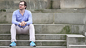 Mann sitzt auf Steintreppe und blickt nach links.