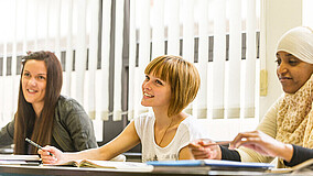 Drei Mädchen sitzen an Schultischen und nehmen am Unterricht teil.