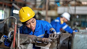 Frau mit Helm arbeitet an einer Maschine