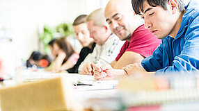 Erwachsene sitzen an Tischen und schreiben