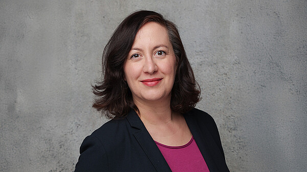 Porträtfoto von Heidi Heberlein. Sie lächelt und blickt in die Kamera. Der Hintergrund ist grau.