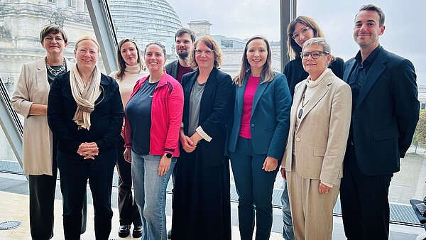 Mehrere Personen stehen zusammen, hinter ihnen ist die Glaskuppel des Deutschen Bundestags in Berlin zu erkennen.