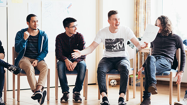 Junge Männer sitzen bei einem Workshop in einer Stuhlreihe.