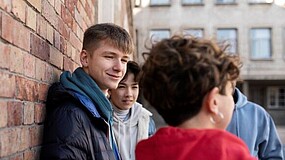 Junge Menschen lehnen an einer Mauer.