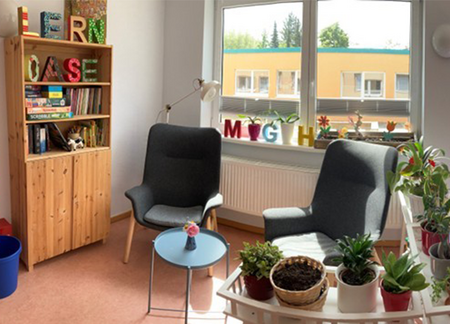 Zwei graue Sessel vor einem Fenster, daneben ein Holzregal mit Büchern und bunten Buchstaben die das Wort "Lernoase" bilden.