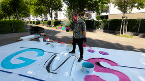 Jannis Plastargias malt den bunten Schriftzug „GUSTAV“ auf die Straße in der Gustavsburgstraße im Frankfurter Gallus.