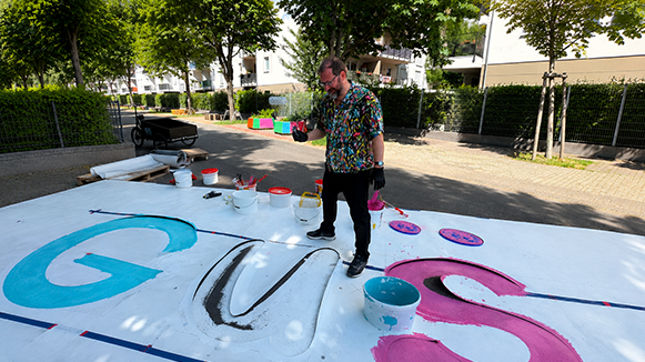 Jannis Plastargias malt den bunten Schriftzug „GUSTAV“ auf die Straße in der Gustavsburgstraße im Frankfurter Gallus.
