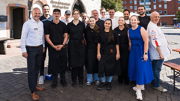 Eine Gruppe von Menschen steht vor einem Gemäuer. Sie lächeln in die Kamera.