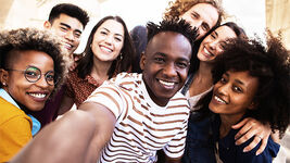 Mehrere junge Menschen mit unterschiedlichen Hautfarben stehen zusammen und lachen.