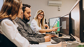 Junge Menschen arbeiten an Laptops und werten statistische Darstellungen aus.