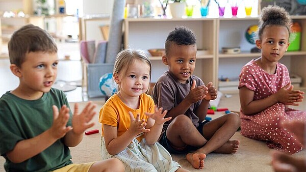 Vier Kinder sitzen auf dem Boden in einem Kreis und klatschen in die Hände