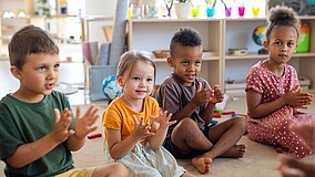 Vier Kinder sitzen auf dem Boden in einem Kreis und klatschen in die Hände