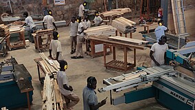 Männer in Arbeitskleidung, teilweise mit Ohrschützern, arbeiten in einer Holzwerkstatt