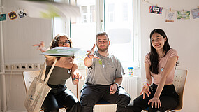 Junge Menschen sitzen in einem Seminar und werfen lachend Unterlagen in die Luft.