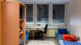 Zimmer einer Schutzwohnung mit Bett, Schreibtisch und Schrank