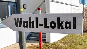 Pfeilschild mit der Aufschrift 'Wahl-Lokal' vor einem Gebäude