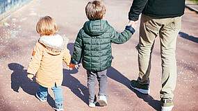 Ein Mann und zwei kleine Kinder sind von hinten zu sehen, während sie zusammen spazieren gehen.