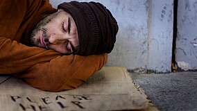 Mann schläft draußen auf einer Pappe