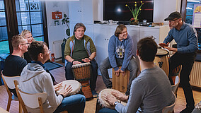 Mehrere Personen sitzen in einem Stuhlkreis und trommeln gemeinsam