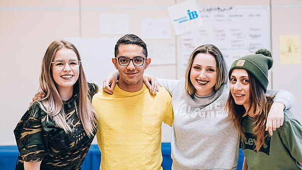 Vier junge Erwachsene lächeln bei einem Workshop des Internationalen Bundes in die Kamera.