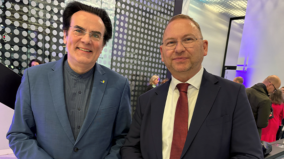 Thiemo Fojkar und Frank Werneke stehen nebeneinander; beide lächeln. Im Hintergrund ist eine Halle mit Menschen.