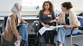 Drei Frauen sitzen auf Stühlen und diskutieren miteinander.. 