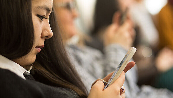 Junge Frau schaut auf ein Smartphone in ihrer Hand.