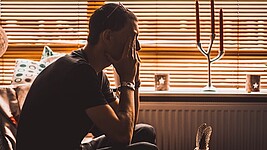 Mann sitzt auf einem Stuhl und bedeckt seinen Augen mit seinen Händen.