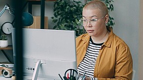 Frau mit kurzen Haaren und Brille sitzt vor einem Monitor.