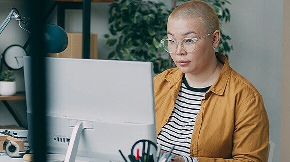 Frau mit kurzen Haaren und Brille sitzt vor einem Monitor.