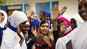 Malala Yousafzai steht lächelnd in einer Gruppe von jungen Frauen.