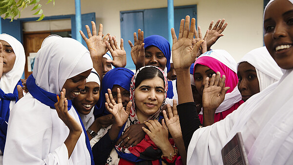 Malala Yousafzai steht lächelnd in einer Gruppe von jungen Frauen.