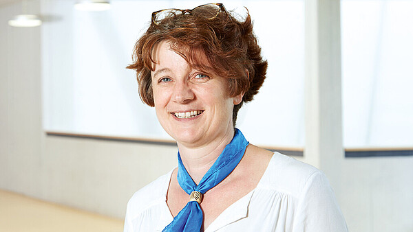 Portrait von Beate Schramm, Schulleiterin beim Internationalen Bund. Sie lächelt in die Kamera und trägt ein blaues Halstuch.