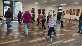 Eine Gruppe Menschen tanzt auf Parkettboden.