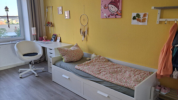 Kinderzimmer mit weißem Bett, Schreibtisch und Drehstuhl vor einer gelb gestrichenen Wand in einer Wohngruppe für Kinder in Burg.