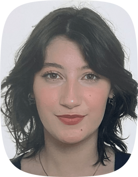 Porträt von Lotta Block: Eine junge Frau mit schulterlangem, gewelltem dunklem Haar, dezentem Make-up und silbernen Ohrringen in Form von Sternen.