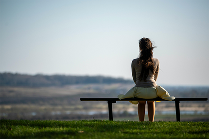 Frau sitzt allein auf einer Bank mit Blick in die Ferne über eine weite Landschaft