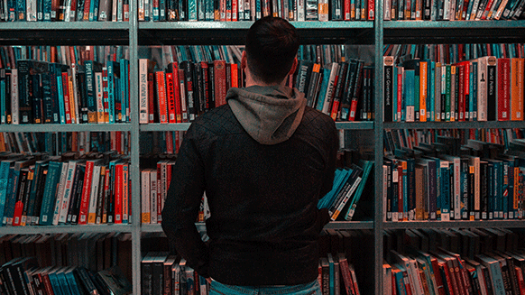 Person steht vor einem Bücherregal in einer Bibliothek.